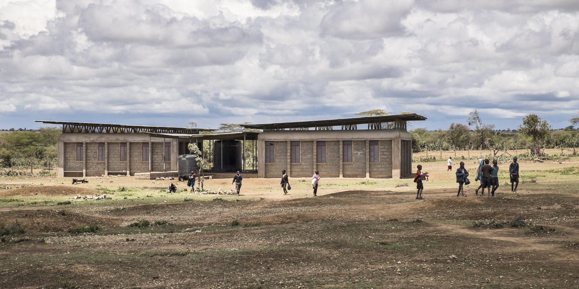 The Oleleshwa Primary School design tackles issues related to durability of Maasai nomadic construction, integration of modern materials, and a focus on natural lighting, natural ventilation, and occupant safety, while respecting the aesthetic of traditional Maasai architecture. Photo of the school from afar.